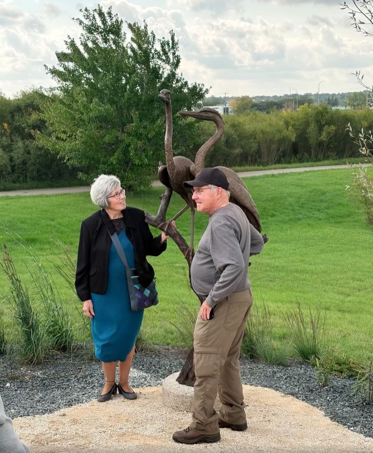 a man and a woman standing near the heron sculpture